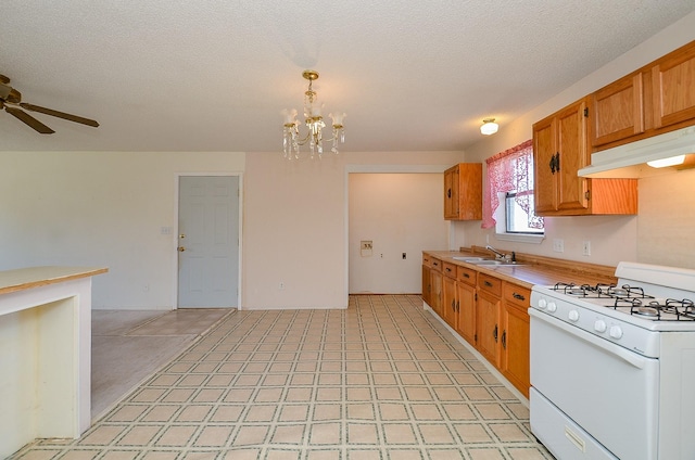 kitchen with white gas stove, a sink, light countertops, under cabinet range hood, and brown cabinets