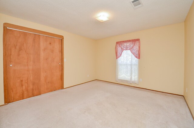 spare room with visible vents, light carpet, a textured ceiling, and baseboards