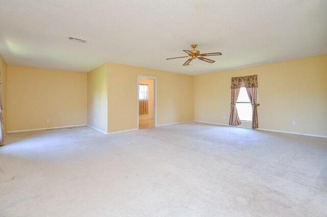 spare room with light carpet, a textured ceiling, baseboards, and a ceiling fan