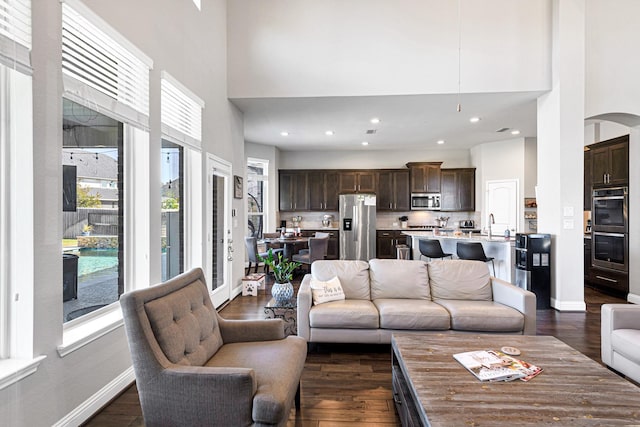 living room with recessed lighting, dark wood-style floors, baseboards, and a towering ceiling