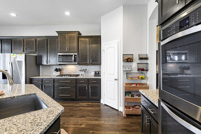 kitchen with dark wood-type flooring, a sink, light stone counters, backsplash, and appliances with stainless steel finishes