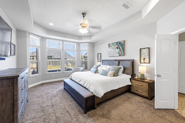 bedroom with a tray ceiling, baseboards, visible vents, and a ceiling fan