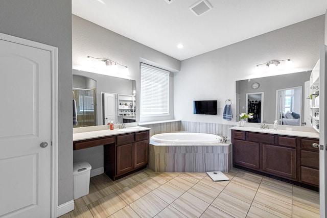 bathroom featuring visible vents, two vanities, a stall shower, a sink, and a garden tub