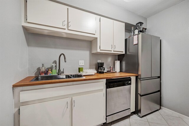 kitchen featuring a sink, wood counters, white cabinetry, appliances with stainless steel finishes, and light tile patterned floors