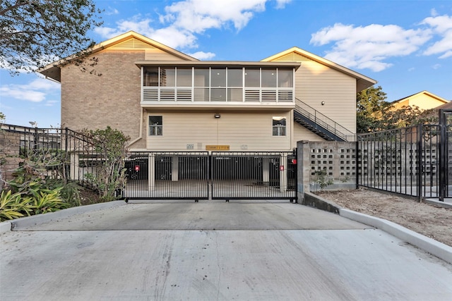 back of house featuring brick siding, a fenced front yard, stairway, a sunroom, and a gate