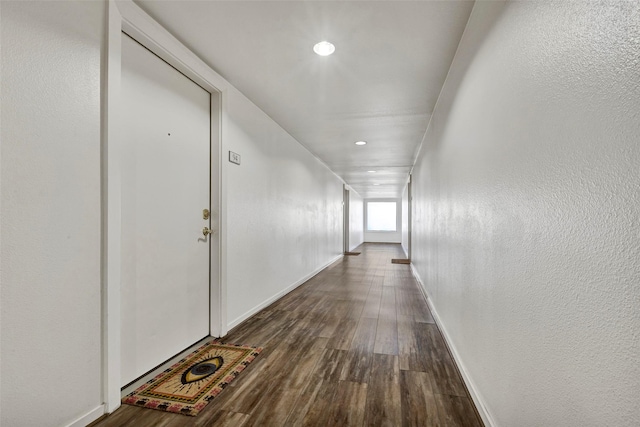 hallway featuring dark wood finished floors, recessed lighting, baseboards, and a textured wall