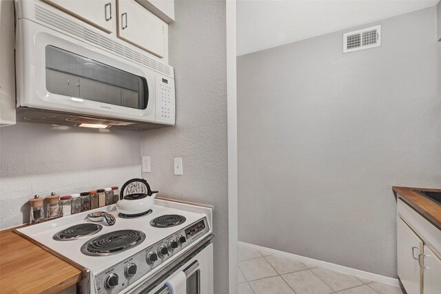 kitchen with white appliances, light tile patterned floors, baseboards, visible vents, and white cabinetry