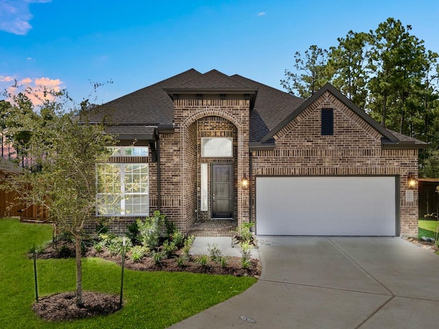 view of front of house with a front yard, a shingled roof, concrete driveway, a garage, and brick siding