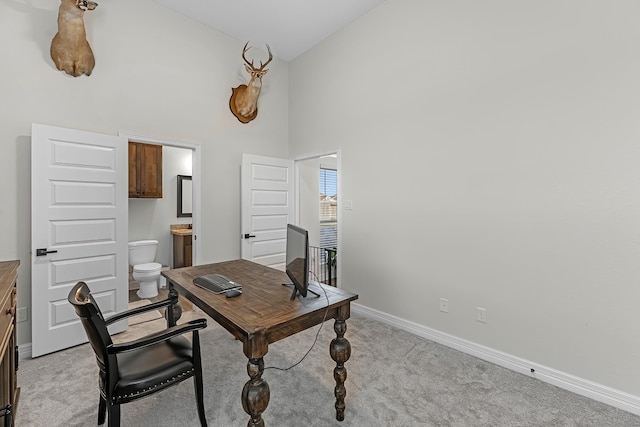 office space featuring light carpet, baseboards, and a towering ceiling