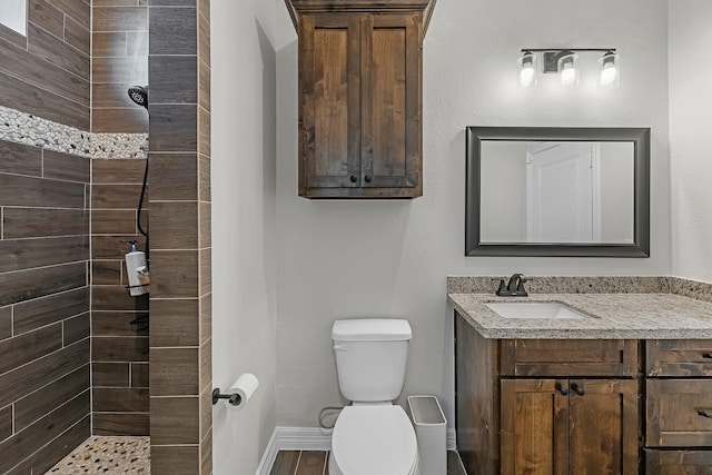 bathroom with baseboards, tiled shower, toilet, and vanity