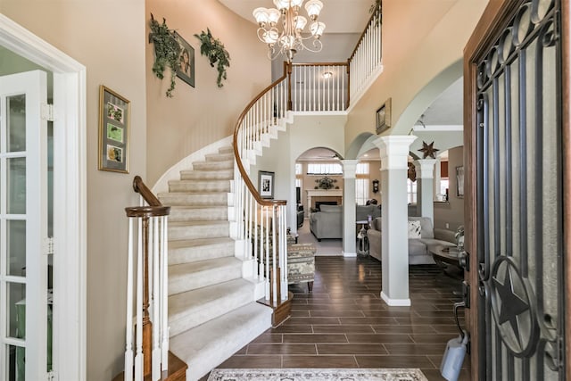 foyer entrance featuring ornate columns, wood tiled floor, arched walkways, stairs, and a tiled fireplace