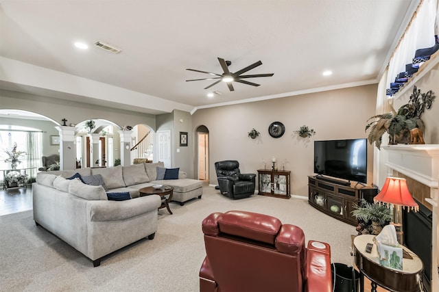 carpeted living room with visible vents, a ceiling fan, stairway, arched walkways, and crown molding