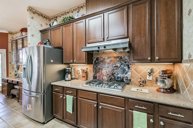 kitchen featuring under cabinet range hood, light stone counters, backsplash, appliances with stainless steel finishes, and light tile patterned flooring