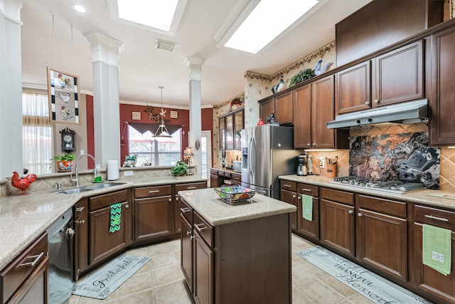 kitchen featuring tasteful backsplash, under cabinet range hood, decorative columns, appliances with stainless steel finishes, and a sink