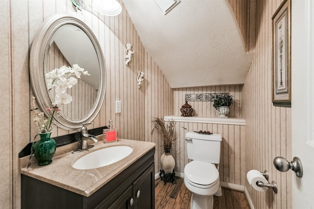 bathroom featuring baseboards, toilet, vanity, wood finished floors, and a textured ceiling