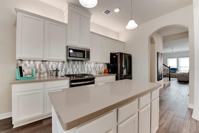 kitchen featuring visible vents, backsplash, wood finished floors, stainless steel appliances, and arched walkways