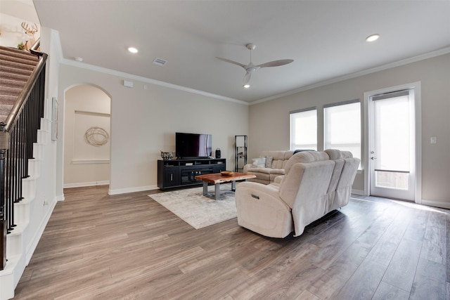 living room featuring visible vents, light wood-style flooring, arched walkways, ornamental molding, and stairs