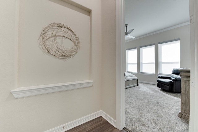 hallway featuring dark carpet, baseboards, and crown molding