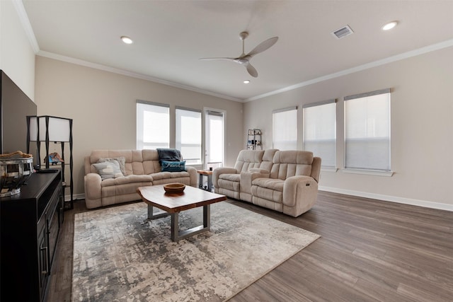 living area featuring wood finished floors, baseboards, visible vents, ceiling fan, and crown molding