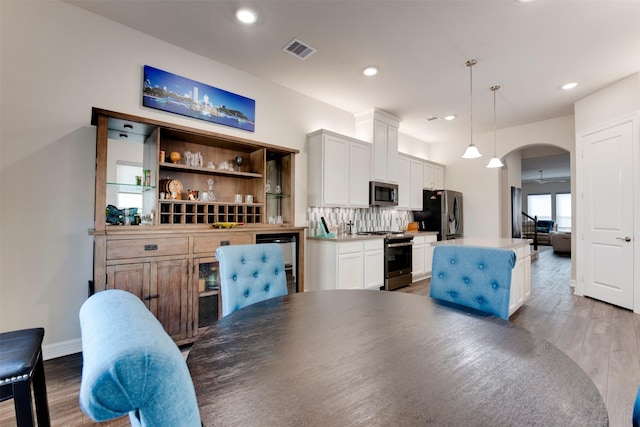 kitchen featuring visible vents, light wood finished floors, a kitchen island, arched walkways, and appliances with stainless steel finishes