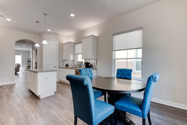 dining space featuring recessed lighting, light wood-type flooring, arched walkways, and baseboards