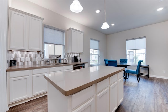 kitchen with wood finished floors, a sink, decorative backsplash, hanging light fixtures, and dishwasher