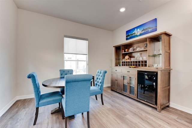 dining space featuring a bar, beverage cooler, baseboards, and light wood finished floors