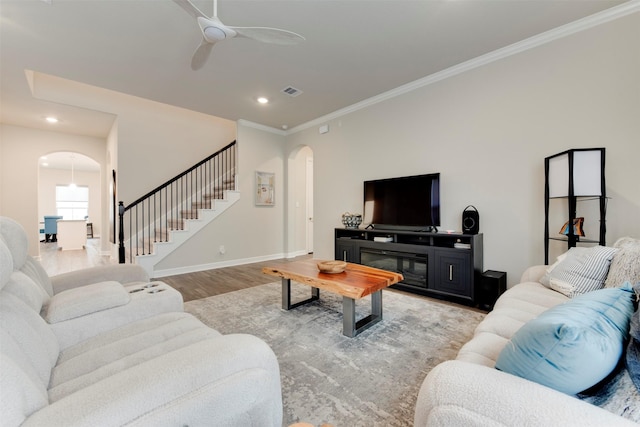 living area with baseboards, light wood-style flooring, arched walkways, ornamental molding, and stairs