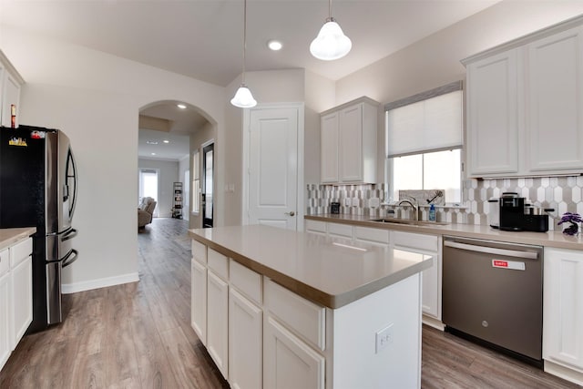 kitchen featuring a kitchen island, arched walkways, a sink, decorative backsplash, and appliances with stainless steel finishes