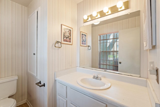 bathroom featuring toilet, wallpapered walls, and vanity