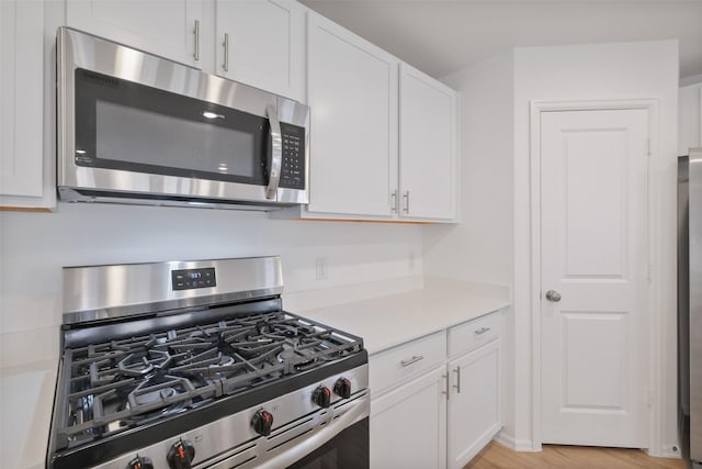 kitchen with light wood finished floors, appliances with stainless steel finishes, light countertops, and white cabinetry