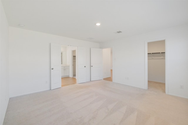 unfurnished bedroom with a walk in closet, recessed lighting, visible vents, and light carpet