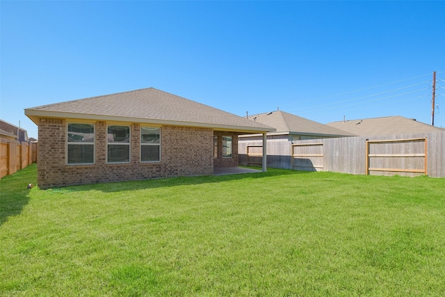 rear view of property with brick siding, a lawn, a shingled roof, and a fenced backyard