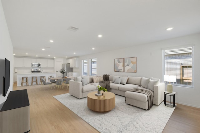 living area with recessed lighting, visible vents, light wood-style flooring, and baseboards