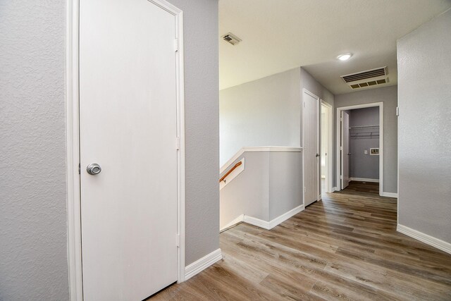 hall featuring wood finished floors, an upstairs landing, visible vents, and baseboards