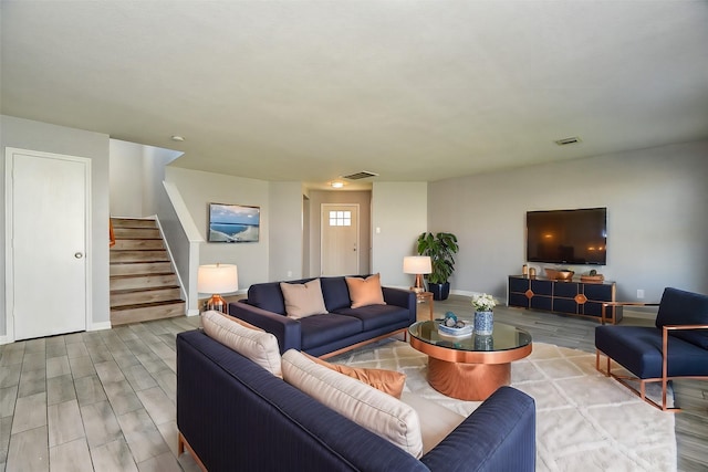 living room with visible vents, baseboards, wood finished floors, and stairway