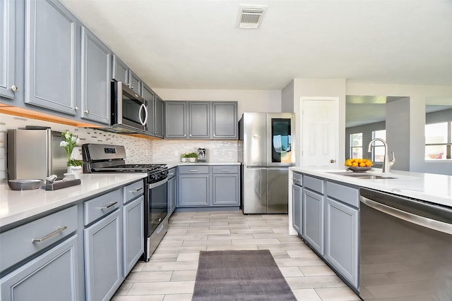 kitchen featuring visible vents, a sink, gray cabinetry, light countertops, and stainless steel appliances