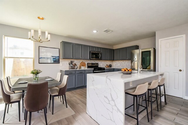 kitchen with light stone countertops, visible vents, gray cabinetry, decorative backsplash, and appliances with stainless steel finishes