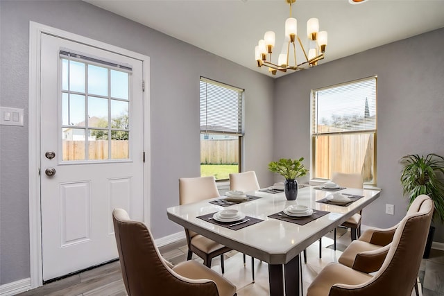 dining space featuring wood finished floors, a notable chandelier, a healthy amount of sunlight, and baseboards