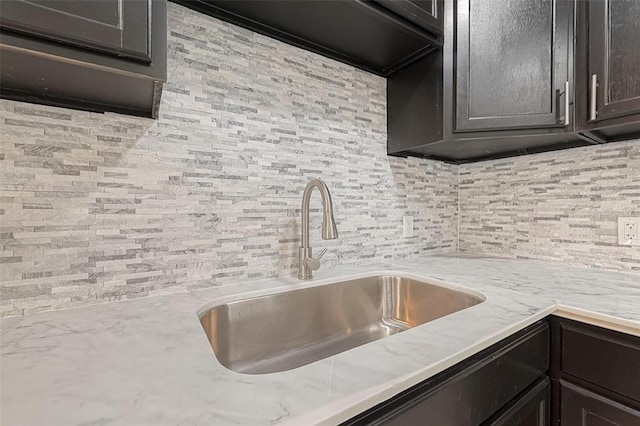 kitchen featuring decorative backsplash, light stone countertops, and a sink