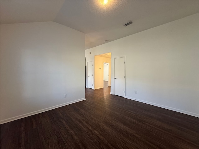 unfurnished room with dark wood finished floors, visible vents, lofted ceiling, and baseboards