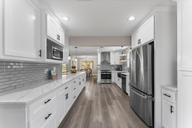 kitchen featuring a sink, wood finished floors, white cabinetry, stainless steel appliances, and wall chimney range hood