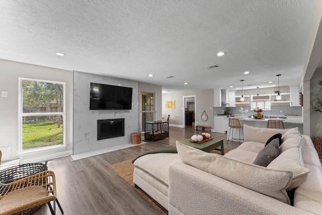 living room with wood finished floors, visible vents, recessed lighting, a high end fireplace, and a textured ceiling