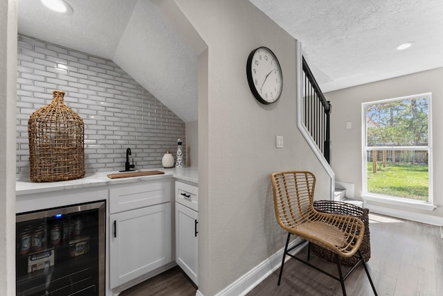 bar featuring beverage cooler, a sink, a textured ceiling, dark wood-style floors, and stairway