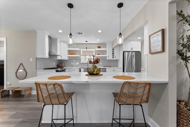 kitchen featuring wall chimney range hood, freestanding refrigerator, wood finished floors, white cabinetry, and open shelves