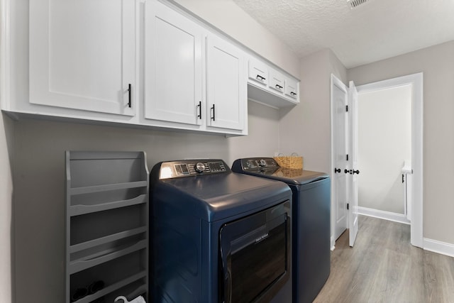 laundry room with baseboards, light wood finished floors, cabinet space, a textured ceiling, and washer and dryer