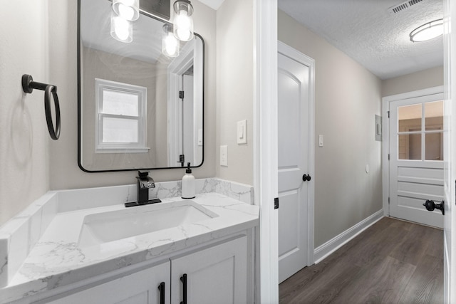 bathroom with visible vents, a textured ceiling, wood finished floors, baseboards, and vanity