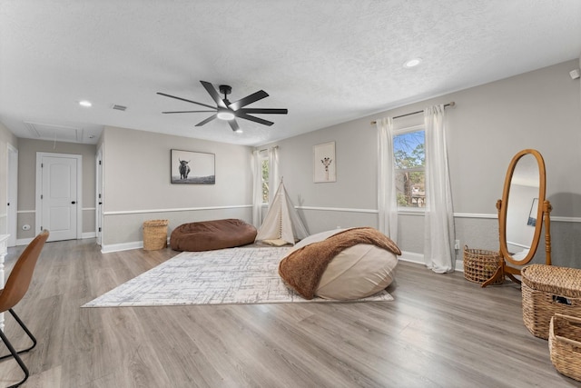 interior space with visible vents, a ceiling fan, a textured ceiling, wood finished floors, and attic access