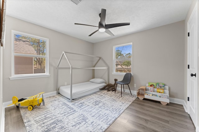 bedroom featuring ceiling fan, baseboards, a textured ceiling, and wood finished floors