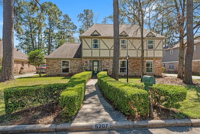 view of front of home with a shingled roof, a front lawn, brick siding, and stucco siding